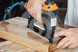carpenter using nail gun or brad nailer tool on wood box in a workshop ,furniture restoration woodworking concept. selective focus