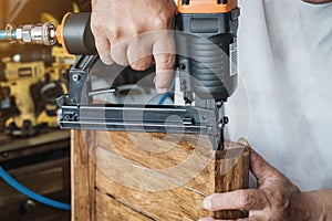 carpenter using nail gun or brad nailer tool on wood box in a workshop ,furniture restoration woodworking concept. selective focus