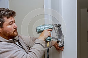 Carpenter using nail gun to moldings on door, framing trim