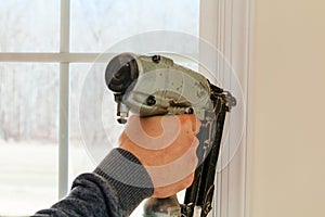 Carpenter using nail gun to moldings on windows, framing trim,