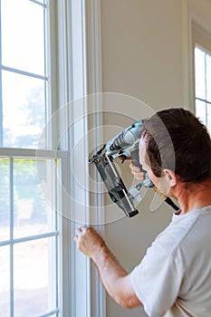 Carpenter using nail gun to moldings on windows, framing trim,