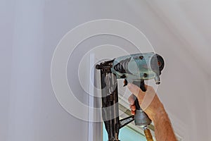 Carpenter using nail gun to moldings on windows, framing trim,