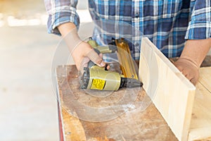 The carpenter using nail gun to nail wood board