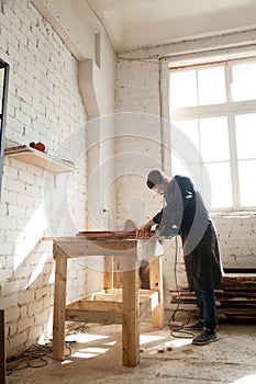 Carpenter using power hand saw cutting wooden planks in workshop