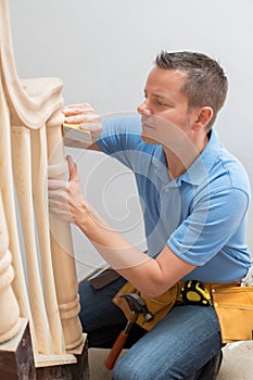 Carpenter Using Sandpaper On Bannister In Home