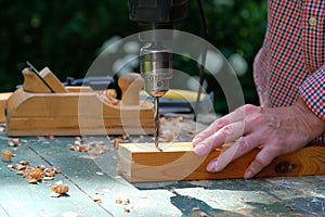 Carpenter woman drilling a hole with an electrical drill in wooden plank, closeup view. Woodwork, DIY, gender equality concept