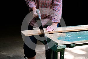 Carpenter woman with handsaw cutting wooden board in workshop. Carpentry, construction, woodworking concept