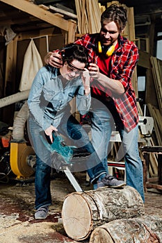 Carpenter woman and man with electric chainsaw in workshop.