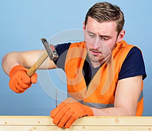 Carpenter, woodworker, builder on concentrated face hammering nail into wooden board. Casual man hammering nail in plank