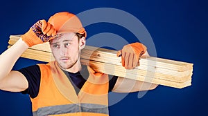 Carpenter, woodworker, labourer, builder carries wooden beam on shoulder. Man in protective gloves holds visor of helmet