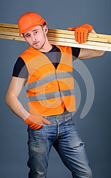 Carpenter, woodworker, labourer, builder on confident face carries wooden beams on shoulder. Man in helmet, hard hat and