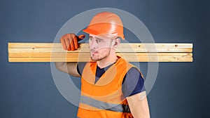 Carpenter, woodworker, strong builder on serious face carries wooden beam on shoulder. Man in helmet, hard hat and