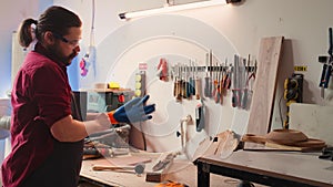 Carpenter in woodworking shop putting on protection gloves