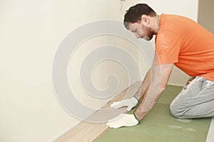 carpenter worker installing wooden laminate or parquet board during flooring work