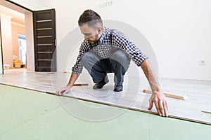 Carpenter worker man installing wood parquet board during flooring work with hammer