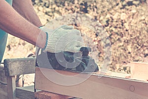 Carpenter working with electric planer on wooden plank