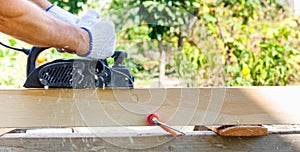 Carpenter working with electric planer on wooden plank