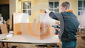 Carpenter working with an electric screwdriver on the factory, fixing wooden furniture details