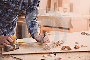 Carpenter working with meter or rule taking measures on wood using pencil. Workshop background