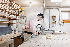 Carpenter working with plane and wood plank at workshop