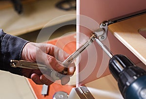 Carpenter working on play furniture. Fixing closers on play kitchen oven door with screwdriver