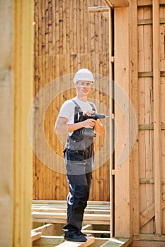 Carpenter working with screwdriver while constructing wooden framed house.