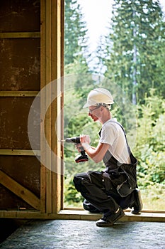 Carpenter working with screwdriver while constructing wooden framed house.