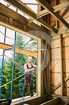 Carpenter working with screwdriver while constructing wooden framed house.