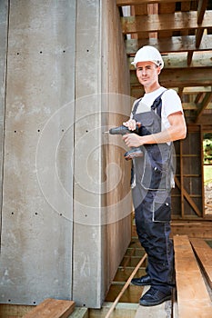 Carpenter working with screwdriver while constructing wooden framed house.