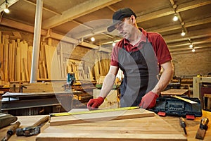 Carpenter working with a wood, marking plank with a pencil and taking measurements to cut a piece of wood to make a piece of