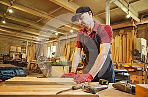 Carpenter working with a wood, marking plank with a pencil and taking measurements to cut a piece of wood to make a piece of