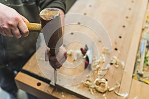 carpenter working on wood by using a mallet and a chisel, workshop, other tools on the wall