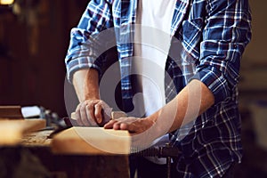 Carpenter works with sandpaper on a wooden plank