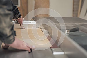 A carpenter works on a woodworking machine. Saws furniture pieces with a circular saw. The process of sawing parts piece