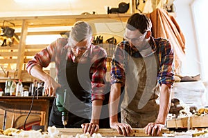 Carpenters with drill drilling plank at workshop