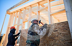 Carpenter hammering nail into OSB panel while building wooden frame house.