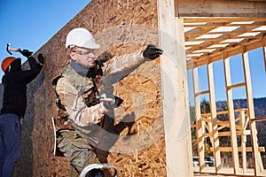 Carpenter hammering nail into OSB panel while building wooden frame house.