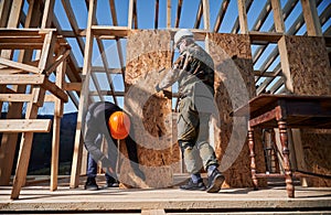 Carpenter hammering nail into OSB panel while building wooden frame house.