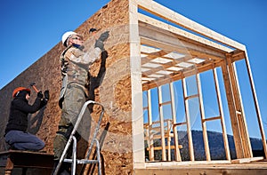 Carpenter hammering nail into OSB panel while building wooden frame house.