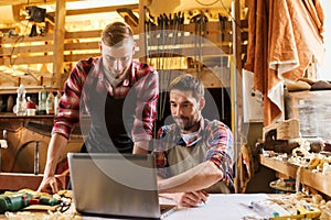 Carpenters with laptop and blueprint at workshop