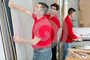 Carpenters moving large sheet plywood in workshop