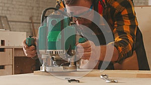 Carpentry industry indoors - man worker in protective glasses and headphones grinding a wooden item in the workshop