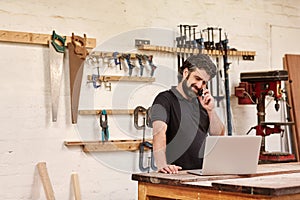 Carpentry small business owner on his phone with a laptop