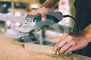 Carpentry is using an electric sander, to smoothen the wood texture. Small business woodworking photo