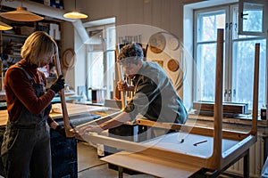 Carpentry workshop, craftsmen working together. Woman and man assembling table, connecting parts