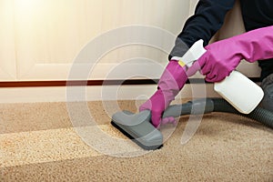 Carpet cleaning concept. cleaner`s hand in gloves sprays cleaning agent on the carpet and vacuums it.