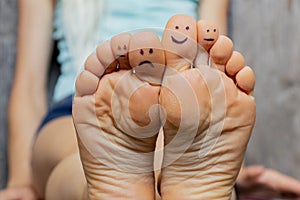 The carpet at home on the floor bare feet of a young girl with a smile and sadness drawn in pencil on her fingers, good mood