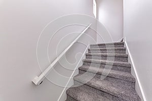 Carpeted stairs with wall-mounted white handrailing upstairs