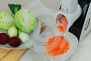 Carrot, beets, onion and cabbage in a vegetable cutter. Chopped carrot is falling into a bowl. Homemade food. Health line