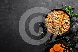 Carrot braised with fresh green peas in creamy milk sauce in stewpan, vegetable saute on black background